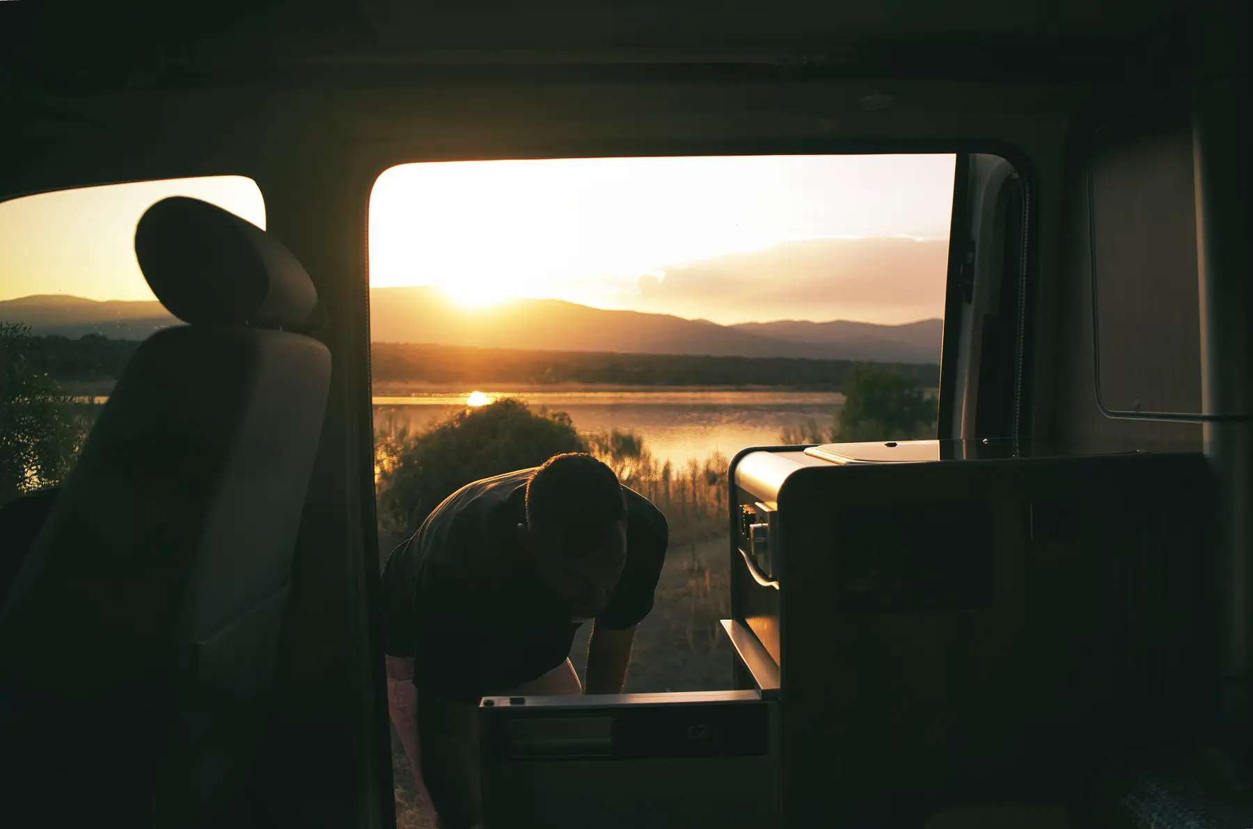 Viajero junto a la nevera de una camper beWinkle con un embalse al atardecer al fondo