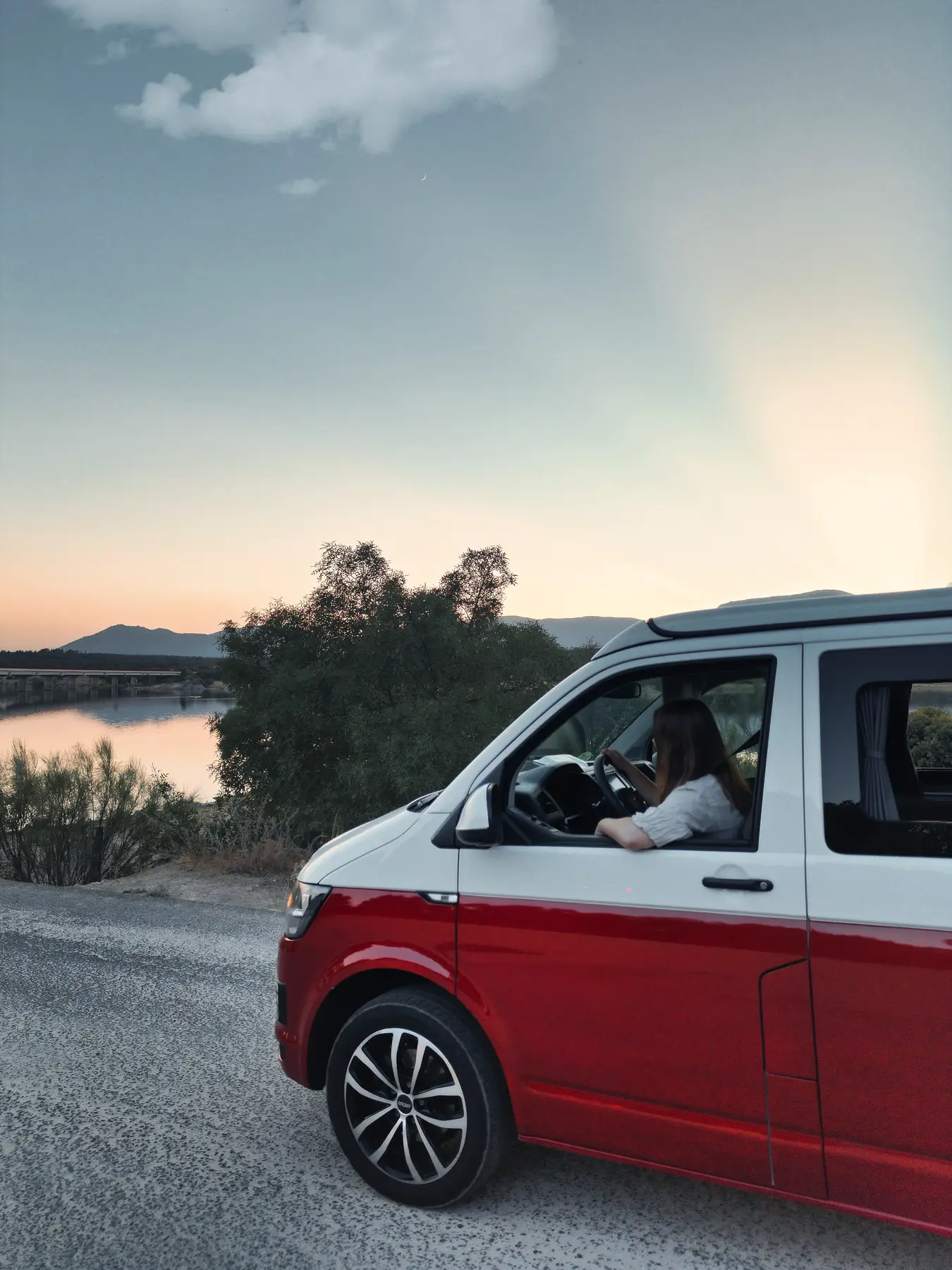 Conductor al volante de una camper beWinkle rodando junto a un embalse al atardecer
